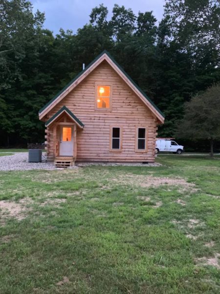 Log cabin with lit windows, surrounded by trees.