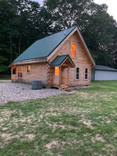 Log cabin with lights surrounded by trees.