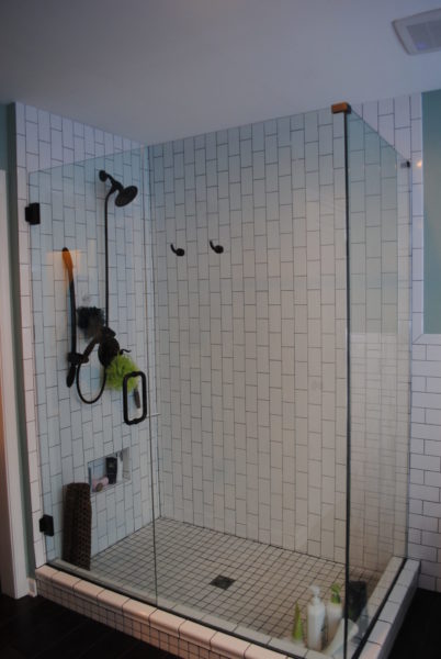 Glass-enclosed shower with black fixtures and tiles.