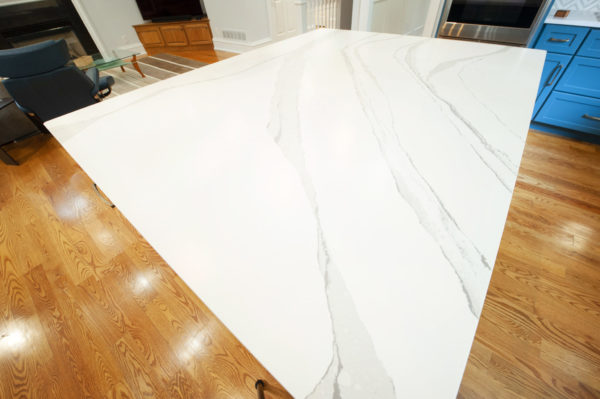 White marble kitchen countertop, wooden floor, blue cabinet.