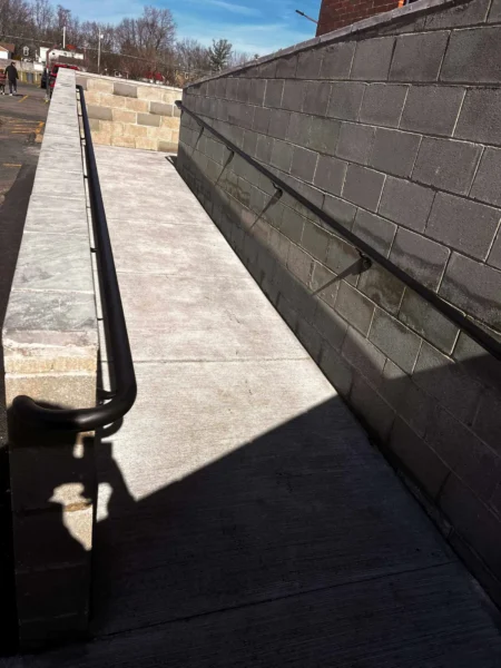 Concrete ramp with metal handrails and shadows.