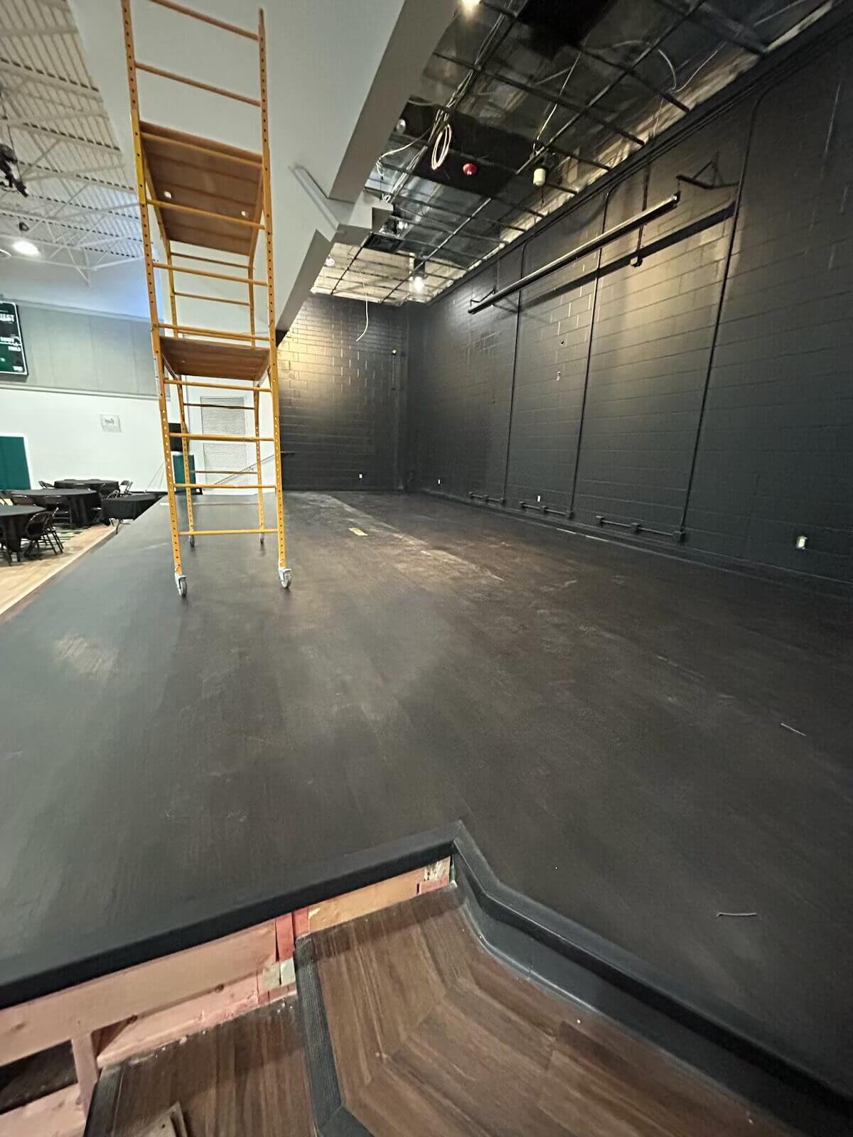 Empty stage with ladder and black walls.