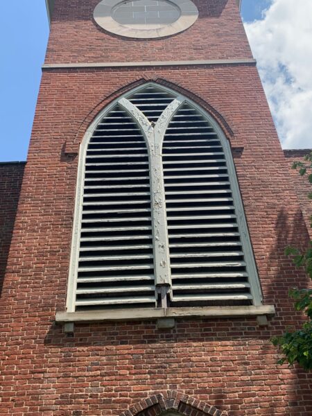 Brick church tower with arched louvered window.